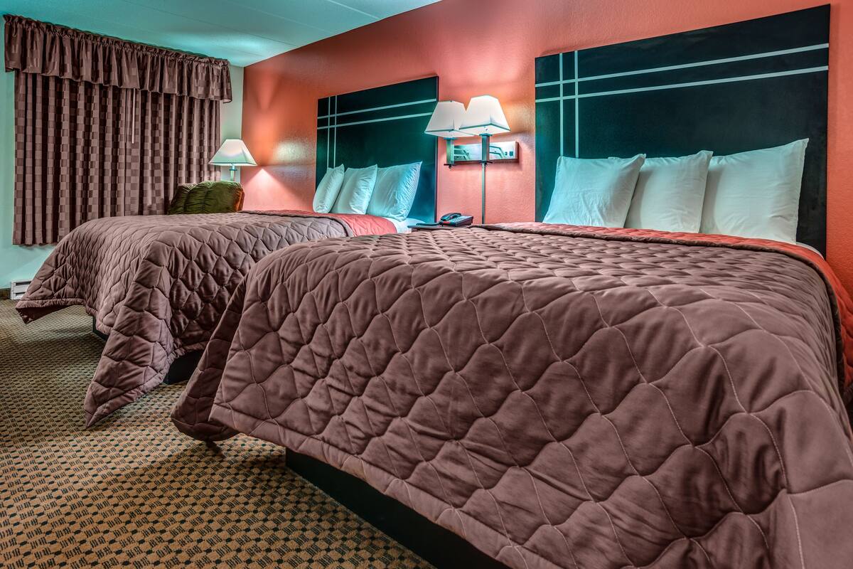 A hotel room with two beds, each with a brown quilted bedspread, a headboard with a grid pattern, and a wall-mounted lamp.