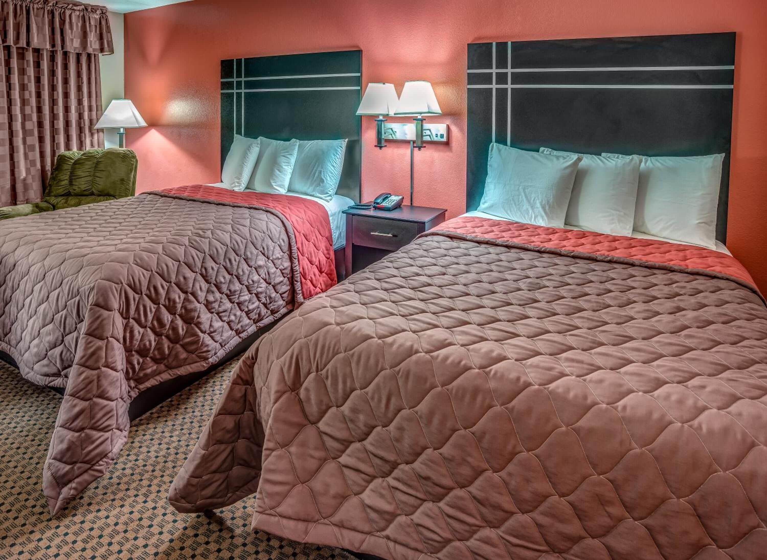 A hotel room with two beds, each with a quilted bedspread, a nightstand with a lamp, and a wall-mounted TV.