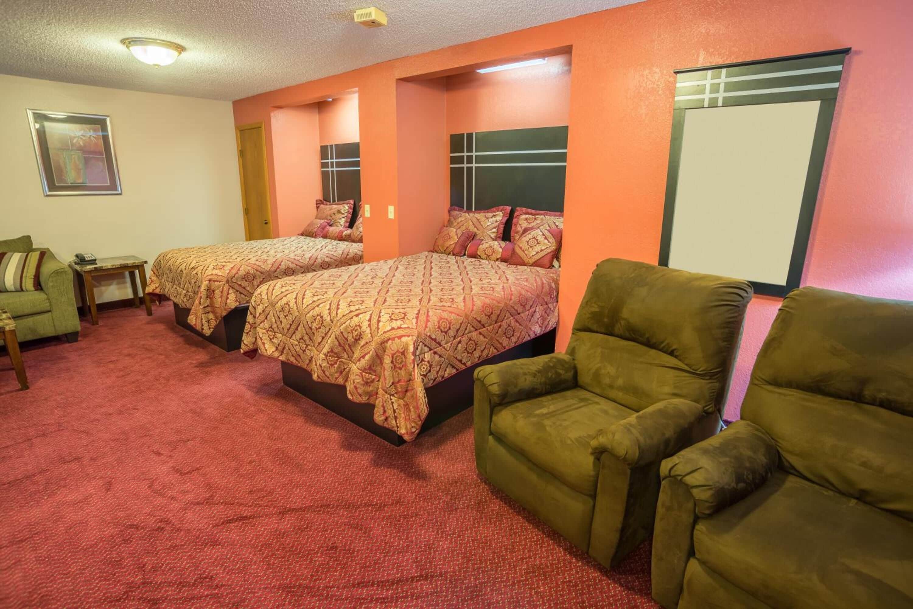 A hotel room with two beds, a green armchair, a small table, and a framed picture on the wall.