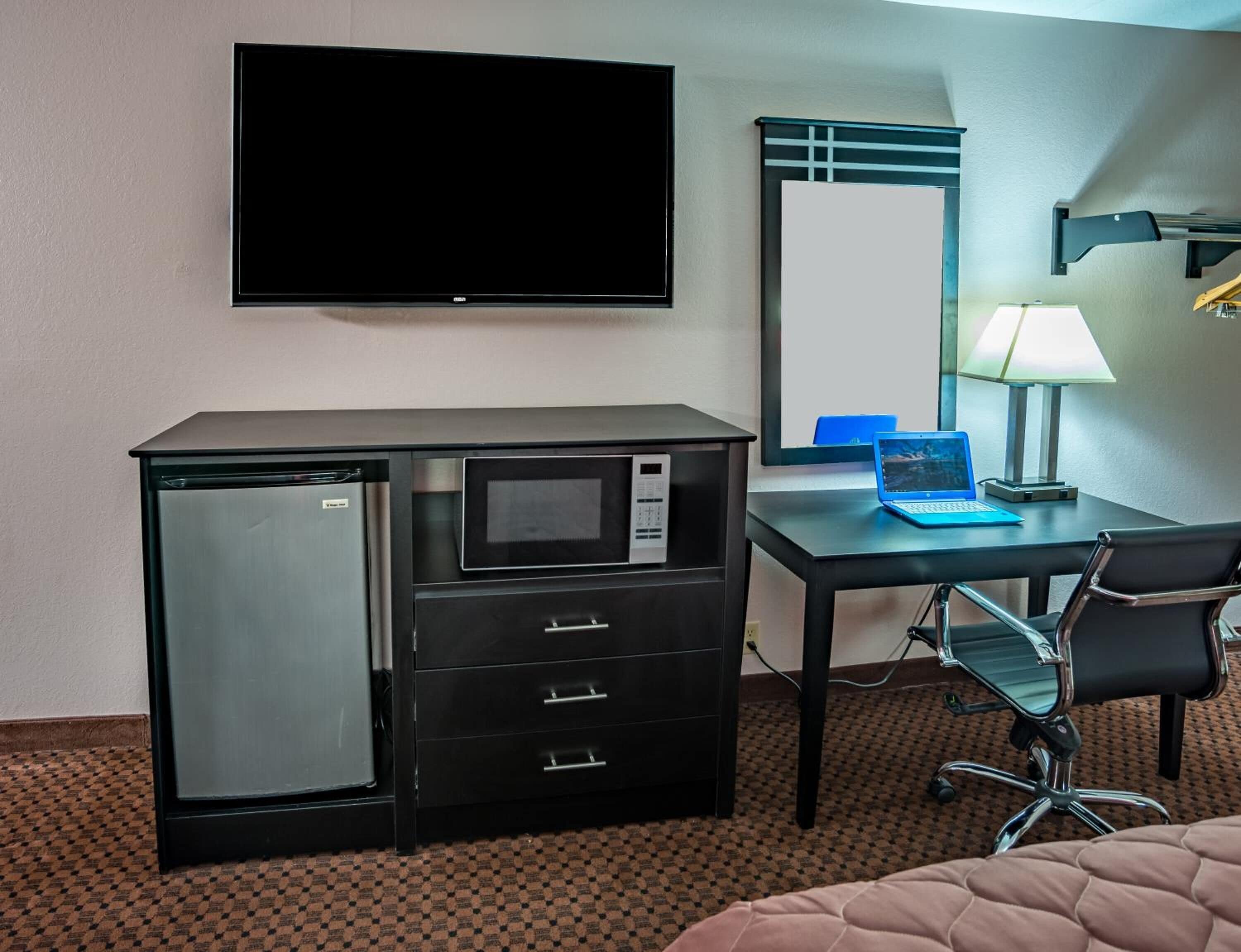 A hotel room with a bed, a desk with a computer, a TV, a microwave, and a refrigerator.