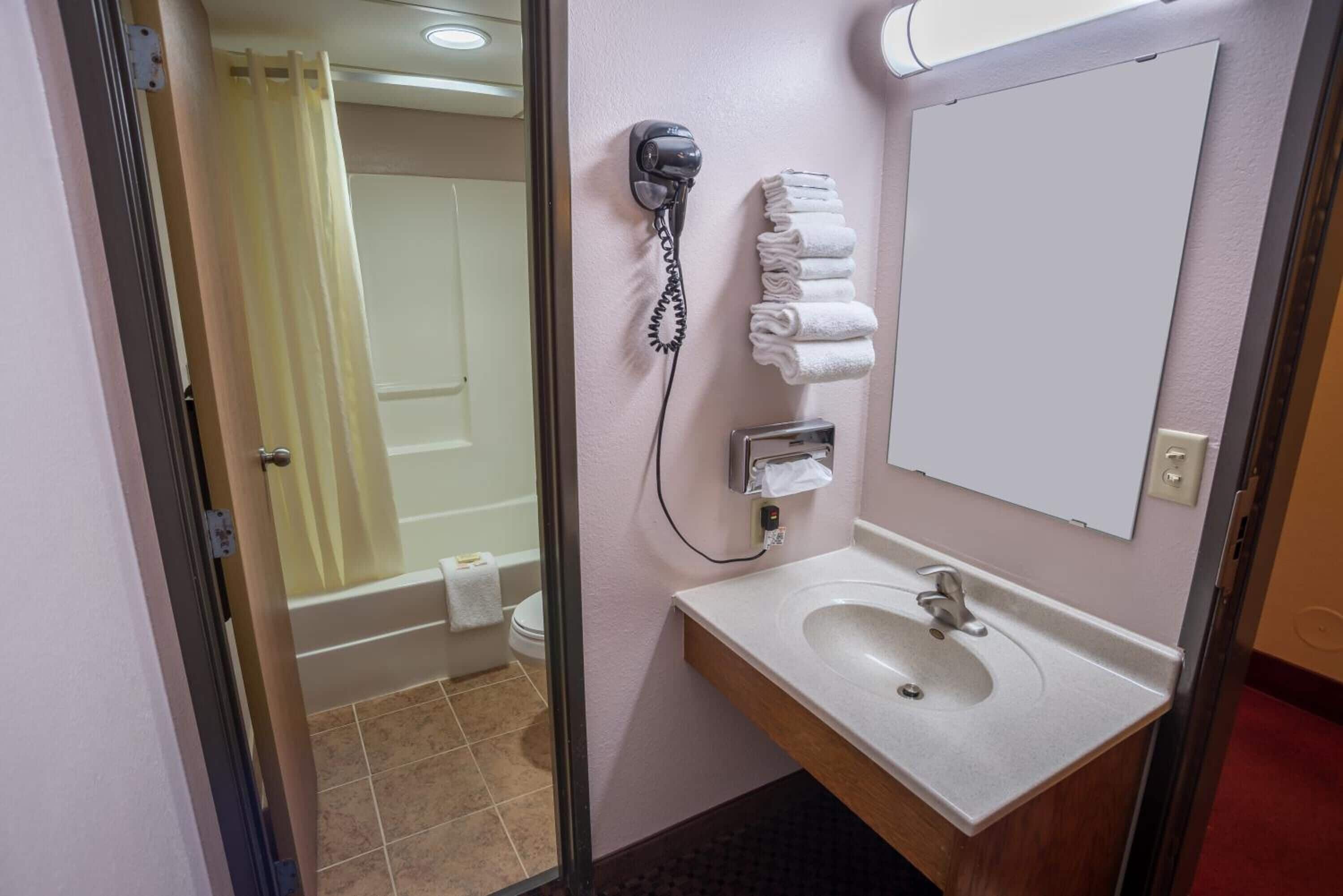 Un baño con lavamanos, espejo, toallero y secador de pelo.
