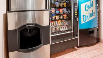 Máquina expendedora con un rótulo que dice 'Bebidas Frías', un dispensador 'Ice-O-Matic' y diferentes bocadillos y bebidas en su interior.
