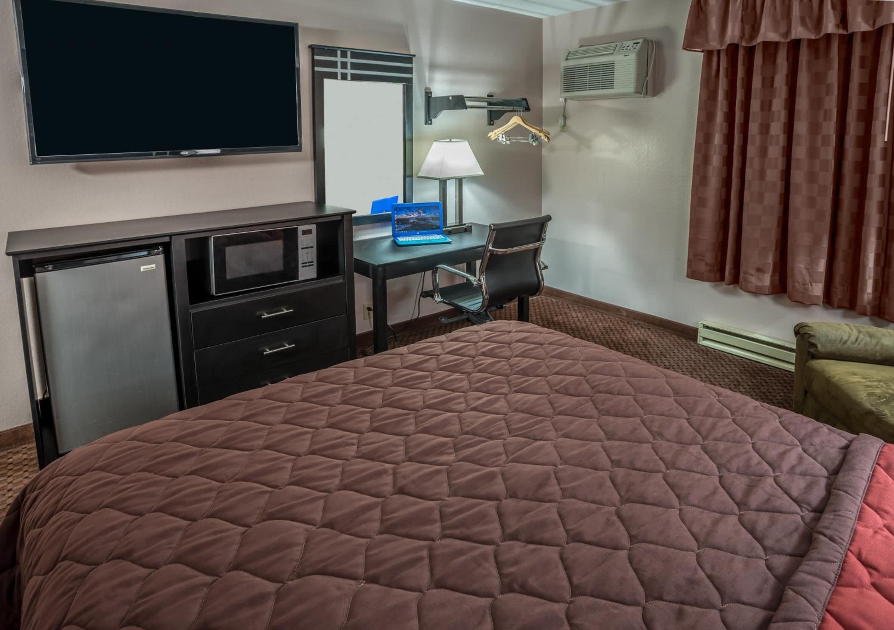A hotel room with a bed, a desk with a laptop, a TV, a microwave, and a wardrobe.