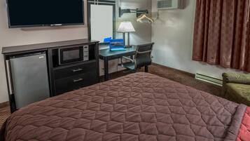 A hotel room with a bed, a desk with a laptop, a TV, a microwave, and a wardrobe.
