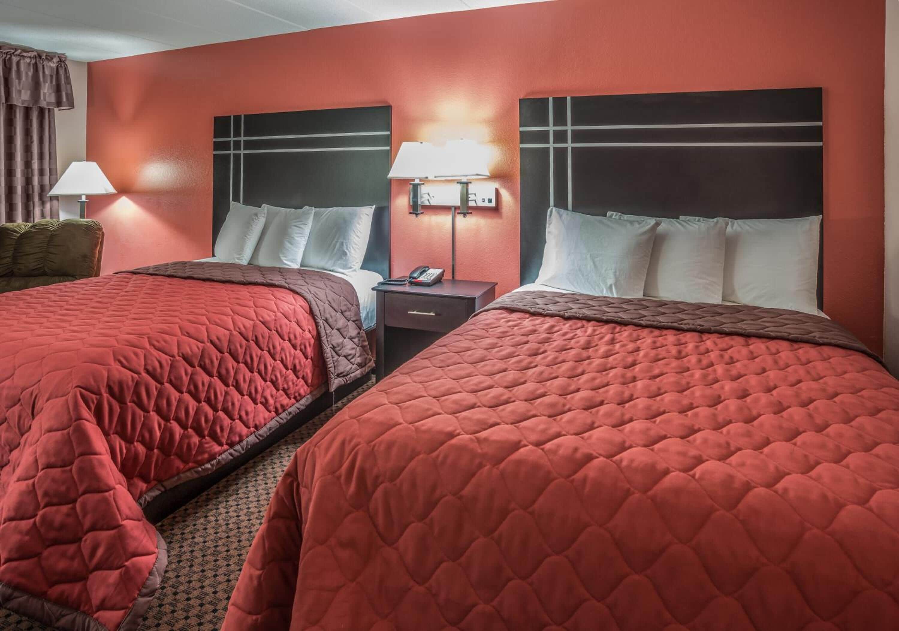 Habitación de hotel con dos camas, cada una con colcha acolchada roja, una mesita de noche con lámpara y teléfono.
