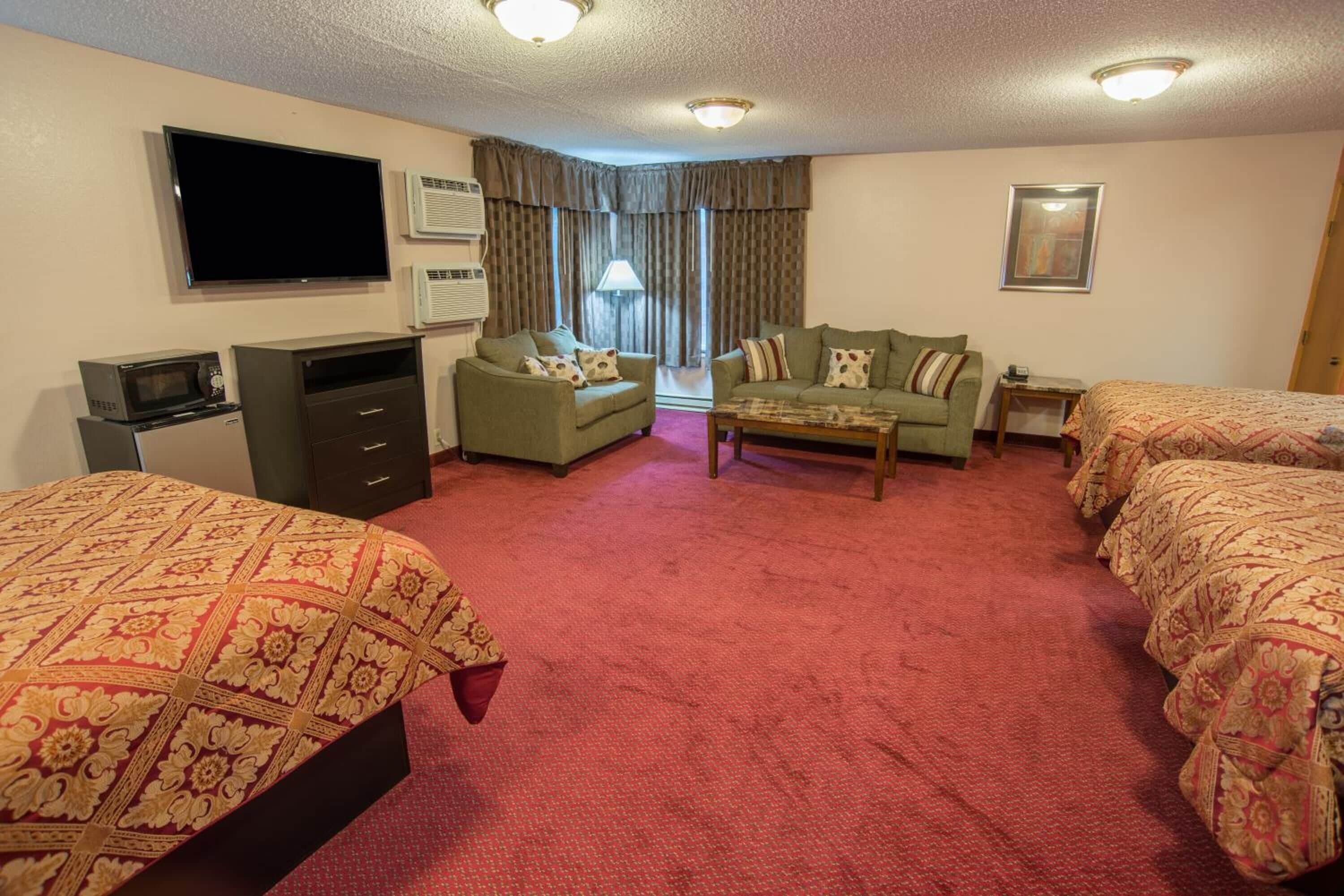 Habitación de hotel con televisión de pantalla plana, microondas, sofá, mesa de centro y dos camas con ropa de cama estampada.