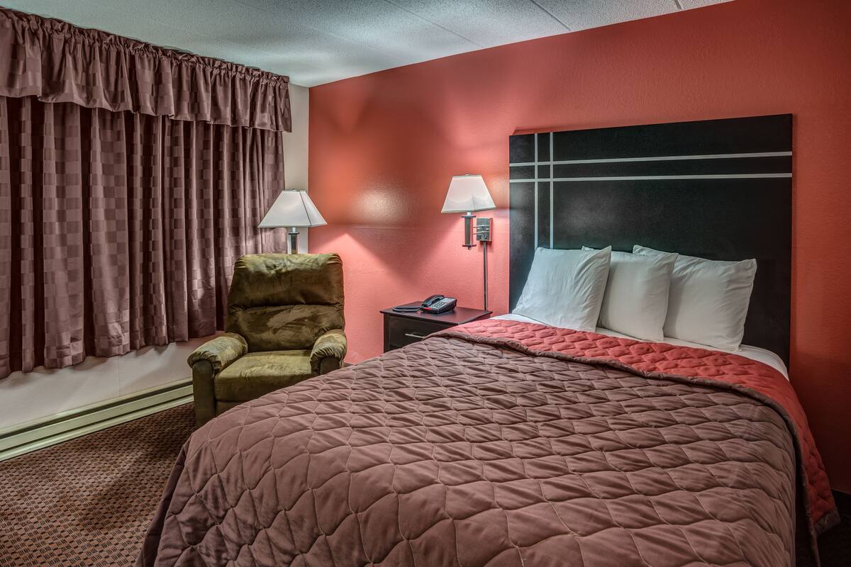 A hotel room with a large bed, a chair, a nightstand with a lamp, and a telephone.