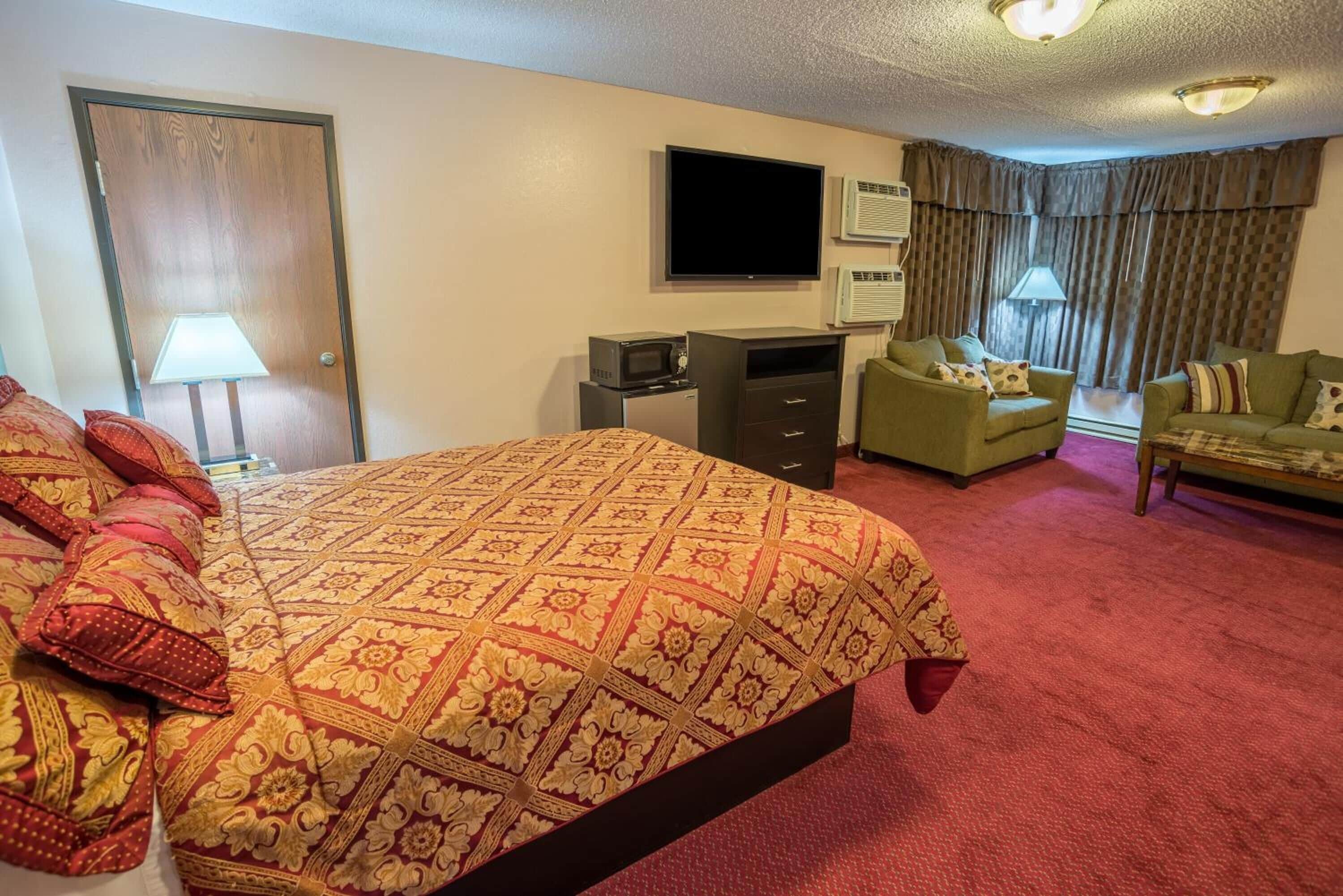 A hotel room with a large bed, a desk with a computer, a TV, and two armchairs.