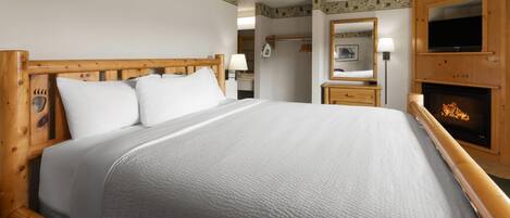 A hotel room with a large bed, wooden headboard, a television, a fireplace, and a mirror.