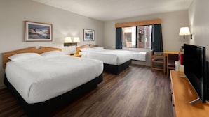Une chambre d’hôtel avec deux lits, un bureau, une télévision et une fenêtre donnant sur un immeuble.