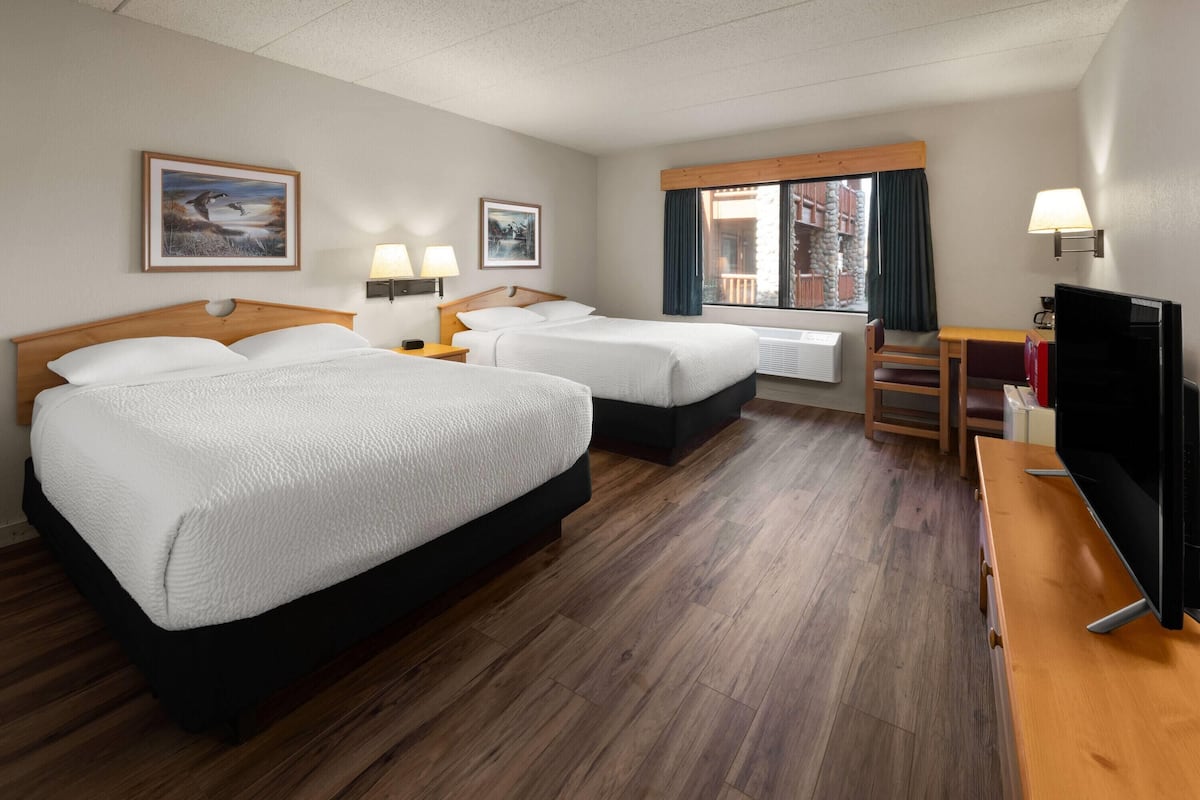 Quarto de hotel com duas camas, uma escrivaninha, televisão e janela com vista para um edifício.