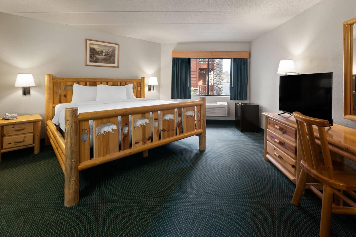 Quarto de hotel com cama de madeira, uma escrivaninha com cadeira, televisão e janela com cortinas.