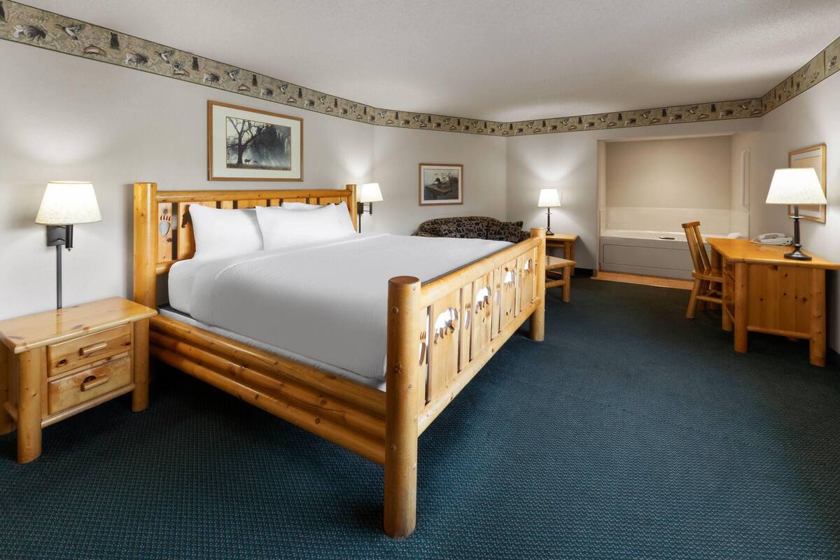 Quarto de hotel com cama de madeira, escrivaninha, cadeira, mesa pequena e banheira.