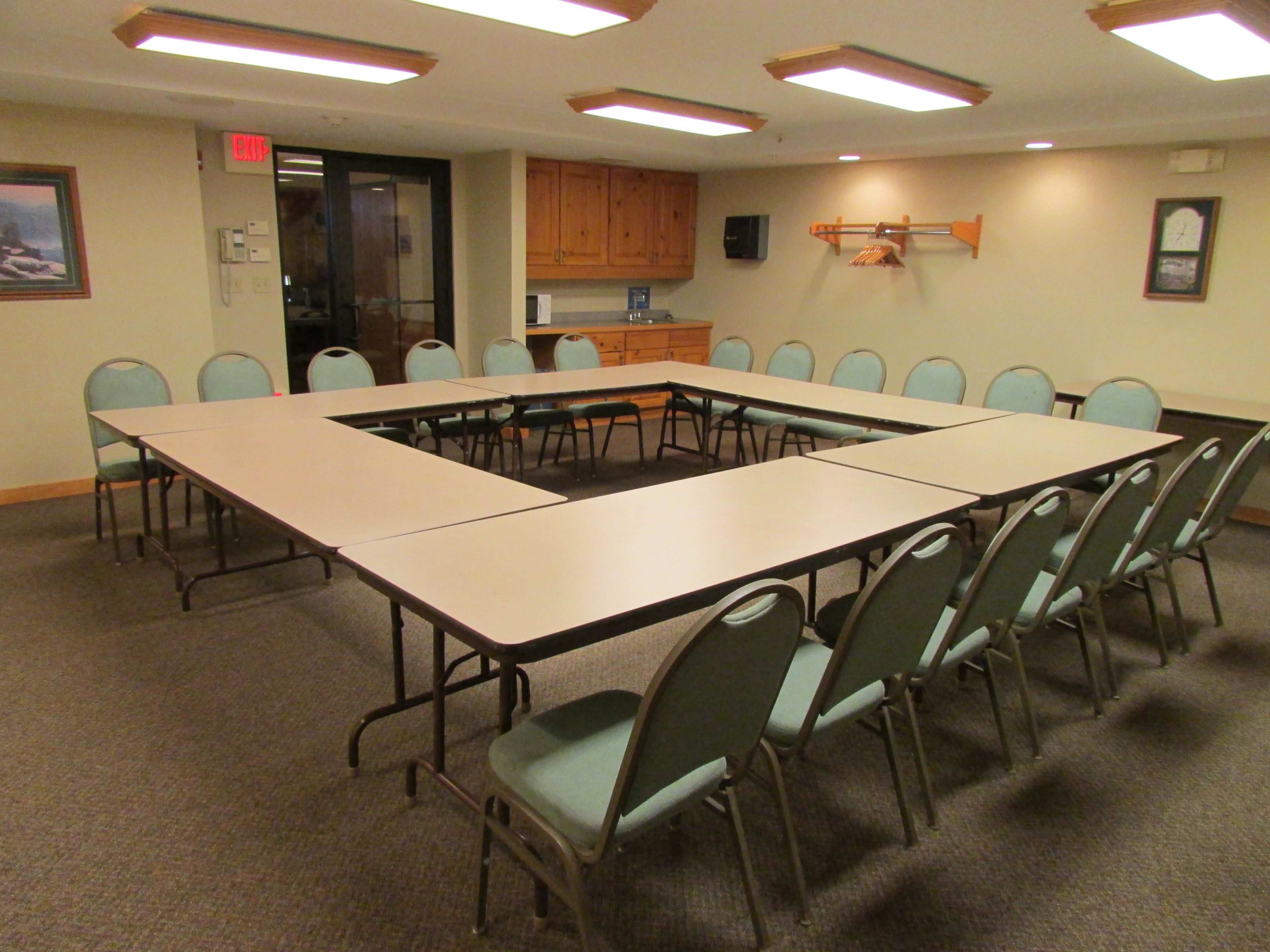 A conference room with a large table and chairs, wooden cabinets, and a clock on the wall.