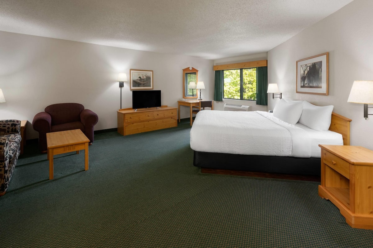 Quarto de hotel com uma cama grande, cómoda de madeira, televis ão, cadeira e secretária.