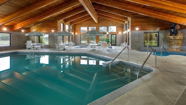 Une piscine intérieure dotée d’un plafond en bois, de murs carrelés, ainsi que de plusieurs chaises longues et de parasols.