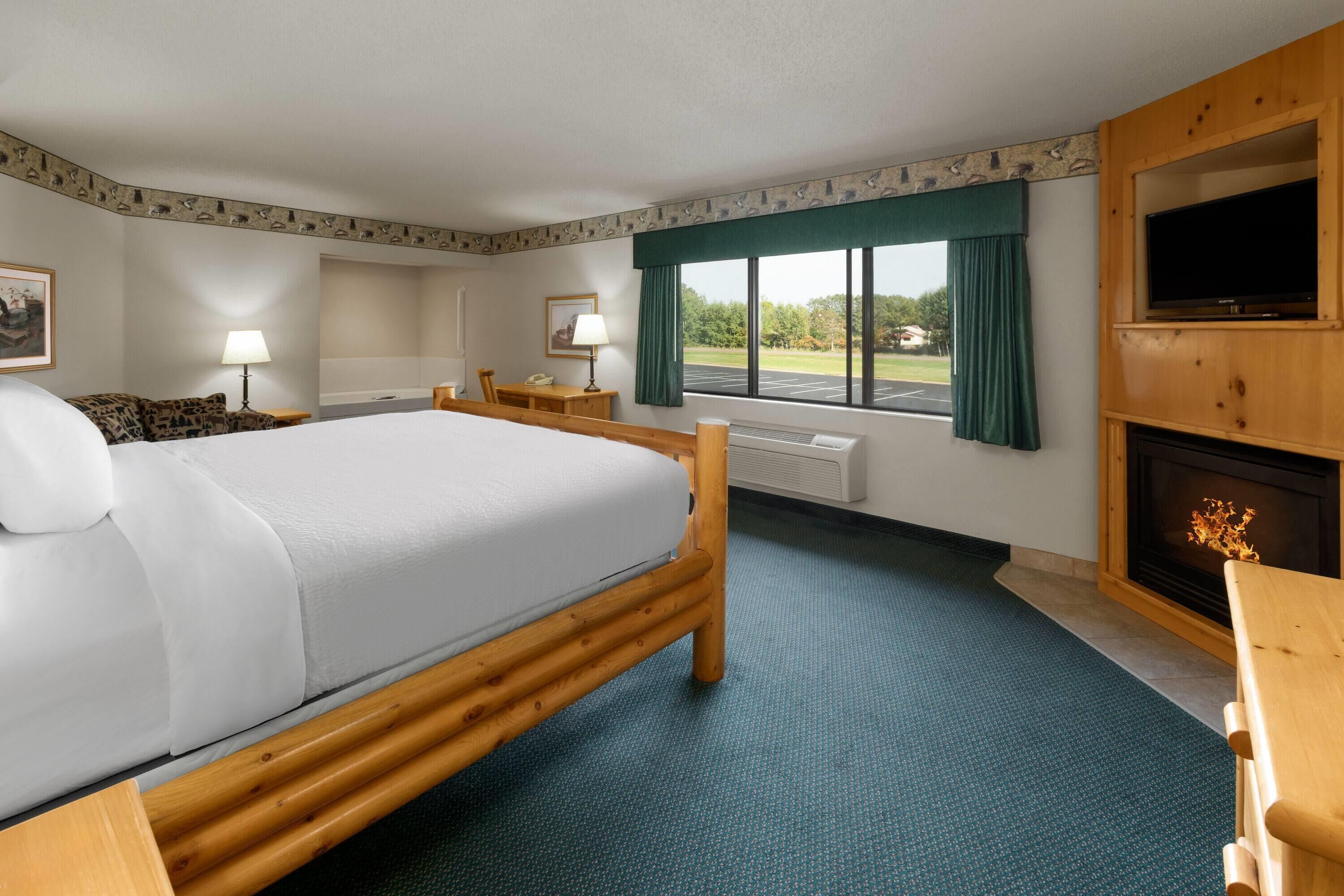 A hotel room with a large bed, a desk, a chair, a television, and a fireplace.