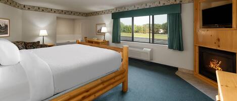 A hotel room with a large bed, a desk, a chair, a television, and a fireplace.