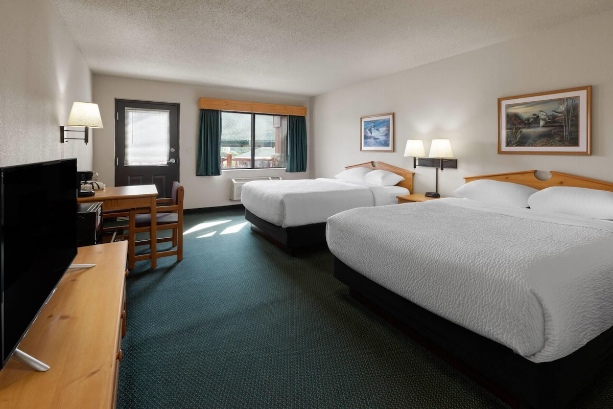 Quarto de hotel com duas camas, uma mesa de trabalho com cadeira, televisão e janela com cortinas.