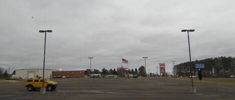 An empty parking lot with a yellow SUV, a gas station, and a flagpole with an American flag.