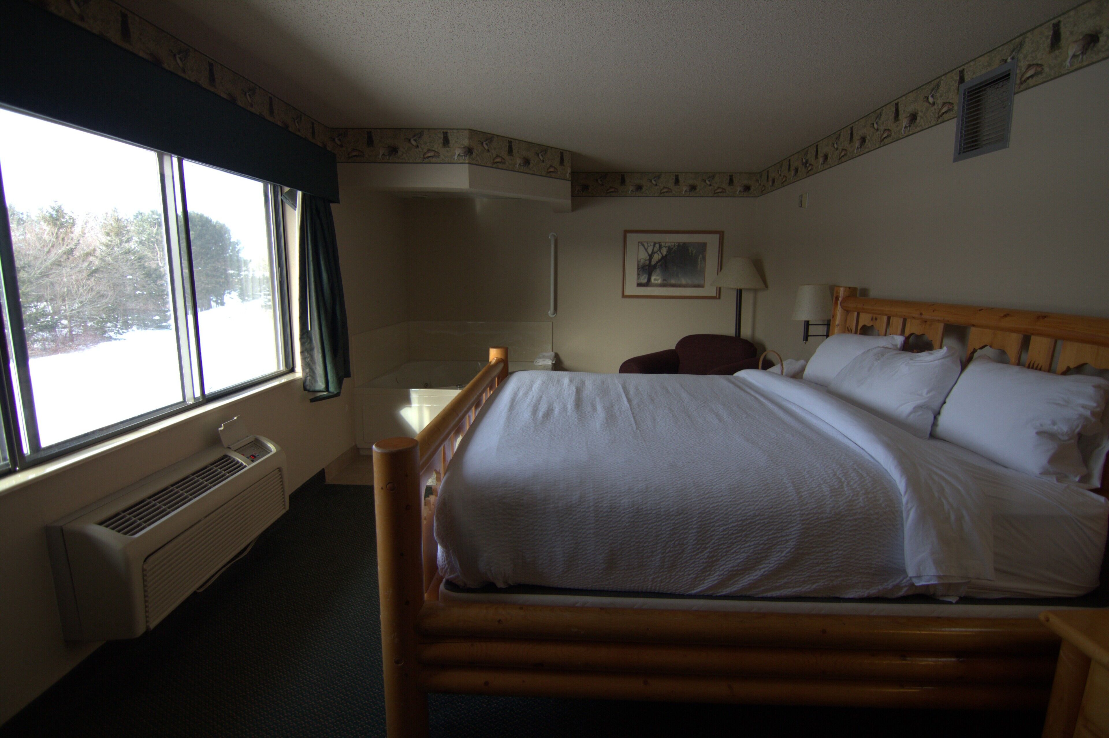 Habitación de hotel con una cama grande, una ventana con cortinas, un radiador, un escritorio con silla y un cuadro en la pared.
