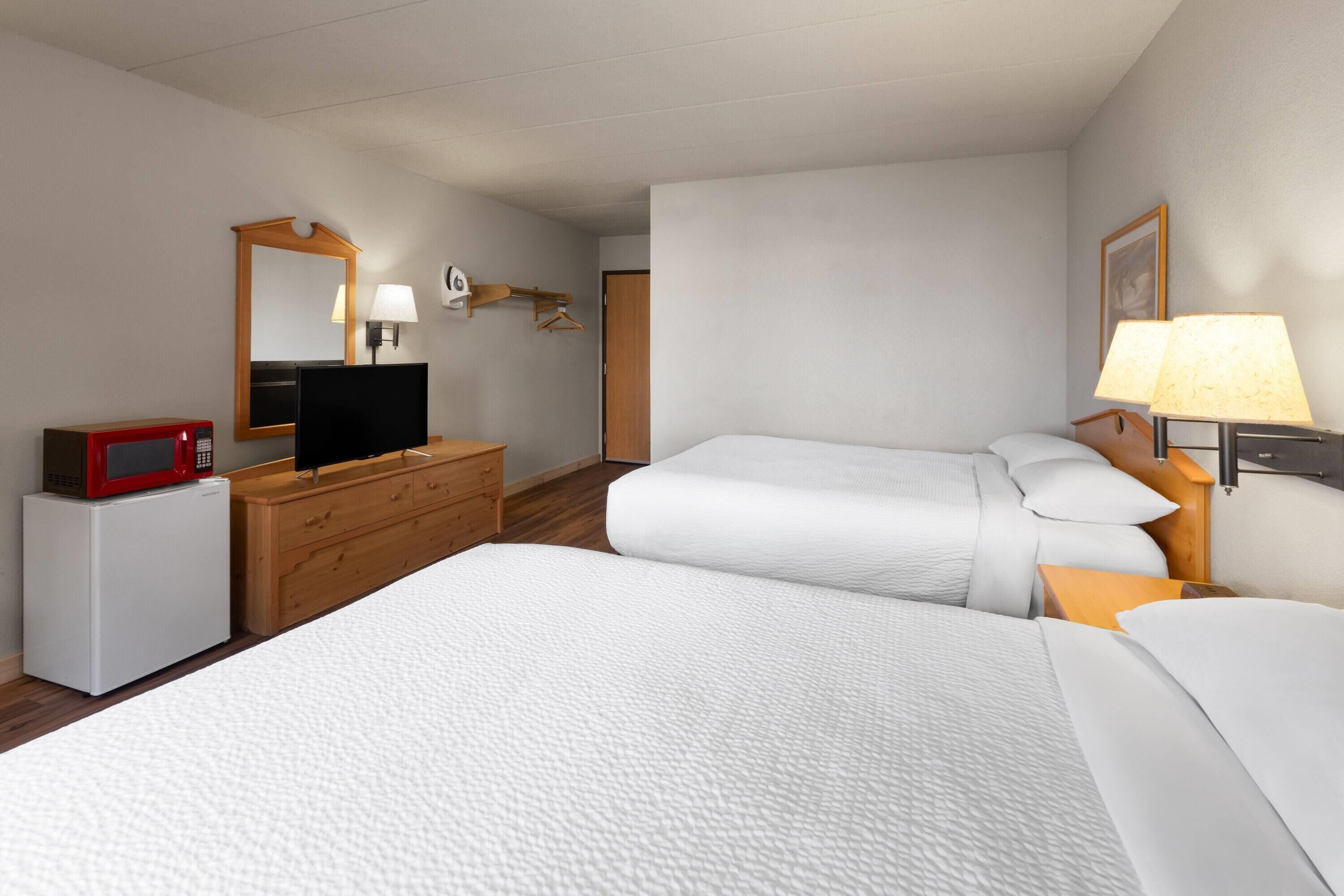 Een hotelkamer met een bed, een dressoir, een magnetron, een televisie en een lamp.