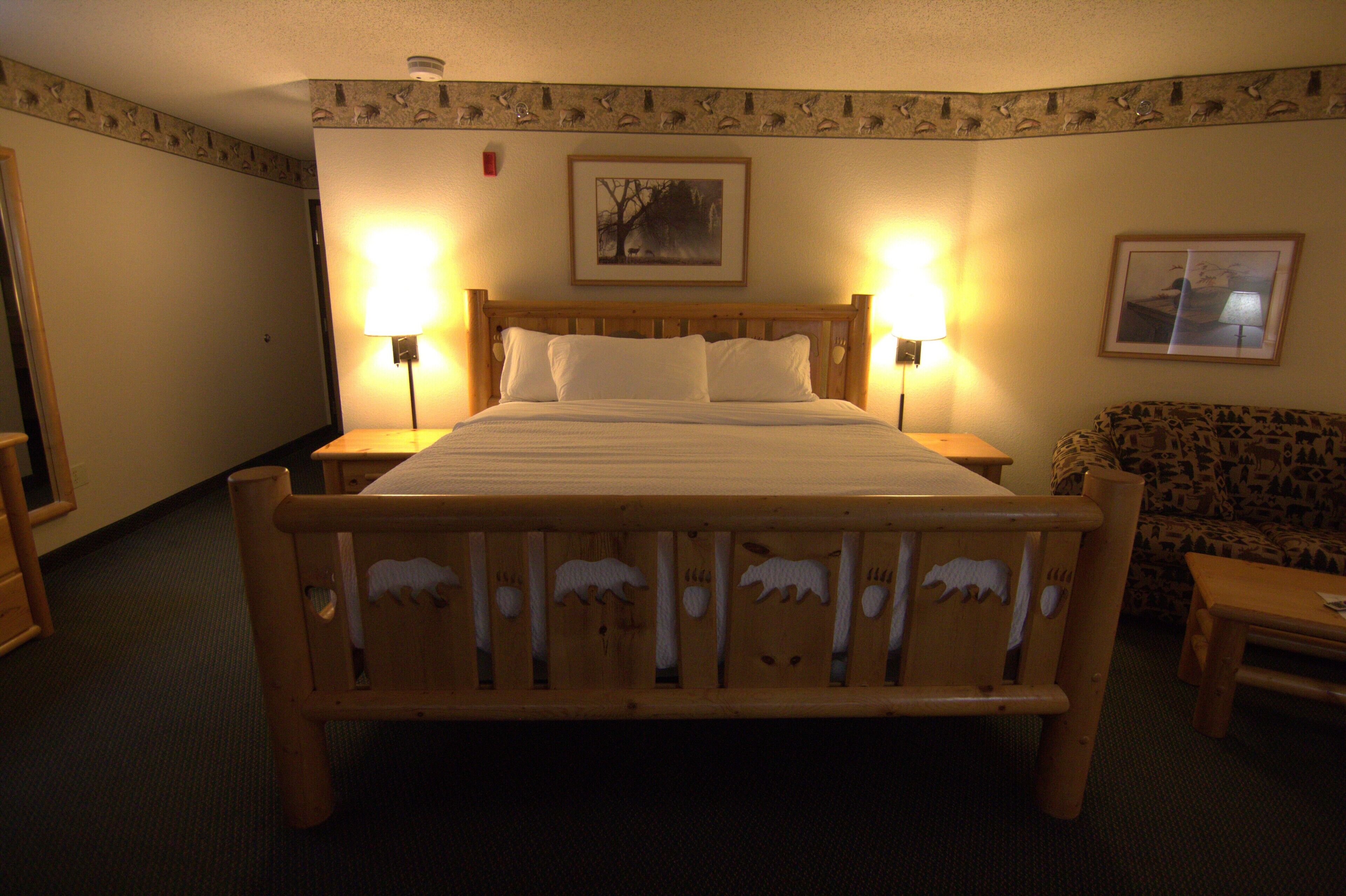 A hotel room with a wooden bed, two bedside lamps, a framed picture on the wall, and a patterned sofa.