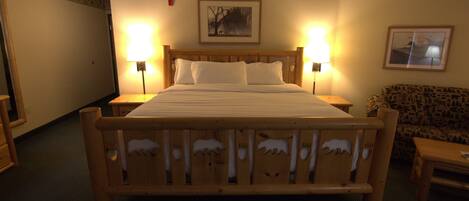 A hotel room with a wooden bed, two bedside lamps, a framed picture on the wall, and a patterned sofa.