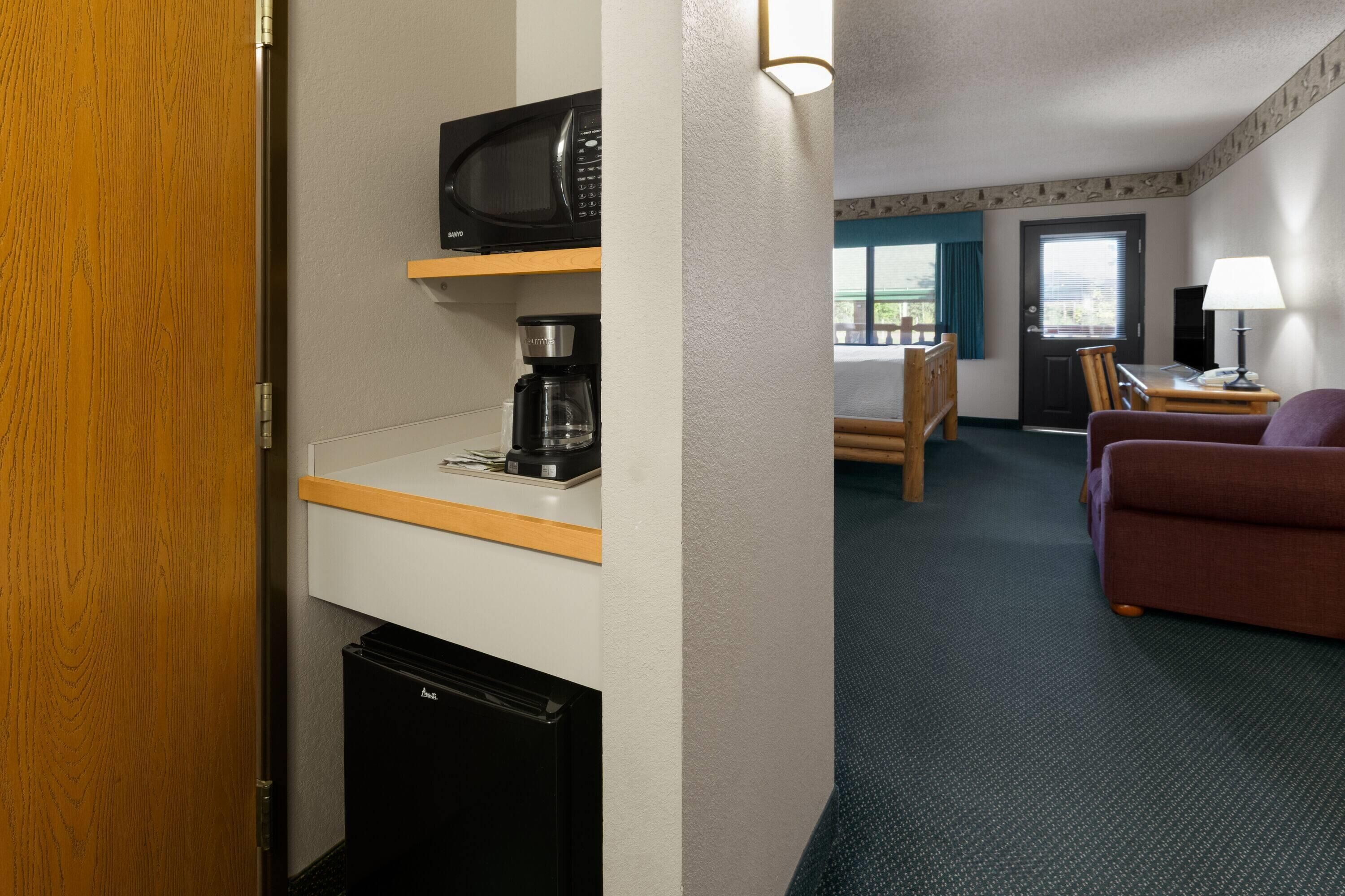 A hotel room with a microwave, coffee maker, and a compact refrigerator. There is a seating area with a couch and a table, and a door leading to a balcony.