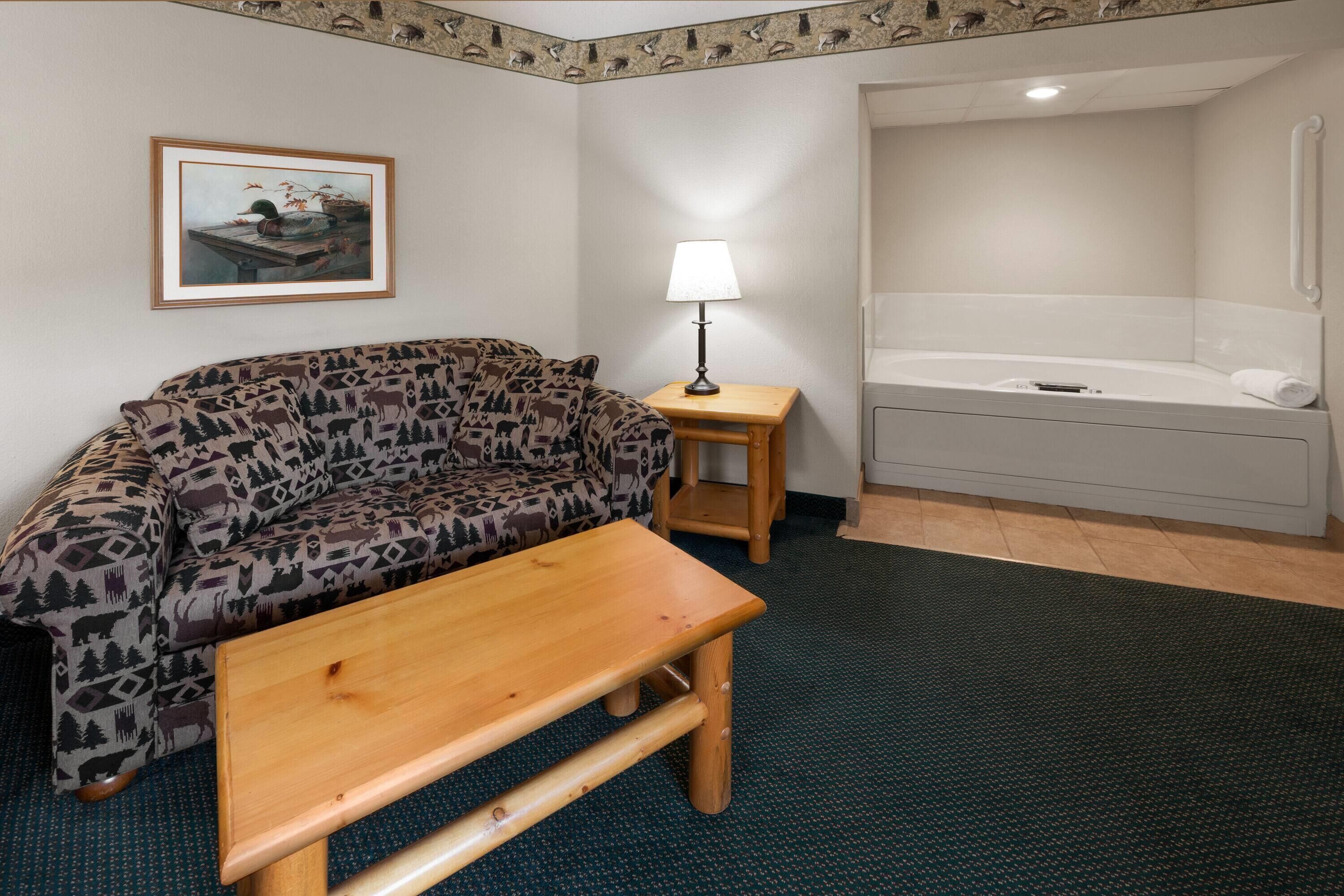 A room with a patterned sofa, a wooden table, a lamp, and a bathtub.