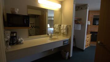 Une salle de bain d’hôtel équipée d’un lavabo, d’un miroir et d’un four à micro-ondes. On y trouve des serviettes suspendues à un porte-serviettes, une poubelle et un meuble en bois avec un miroir.