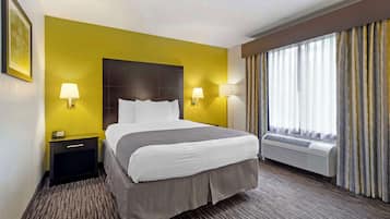 Una habitación de hotel con cama, dos lámparas de noche, mesita de noche, ventana con cortinas y un equipo de aire acondicionado.