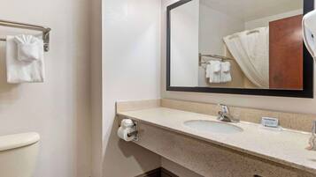 A bathroom with a toilet, sink, and mirror. There are towels hanging on a rack and a sign on the sink.
