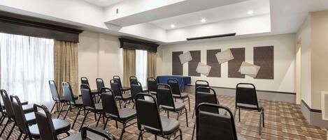 A conference room with foldable chairs arranged in rows, a blue table, and a patterned carpet.
