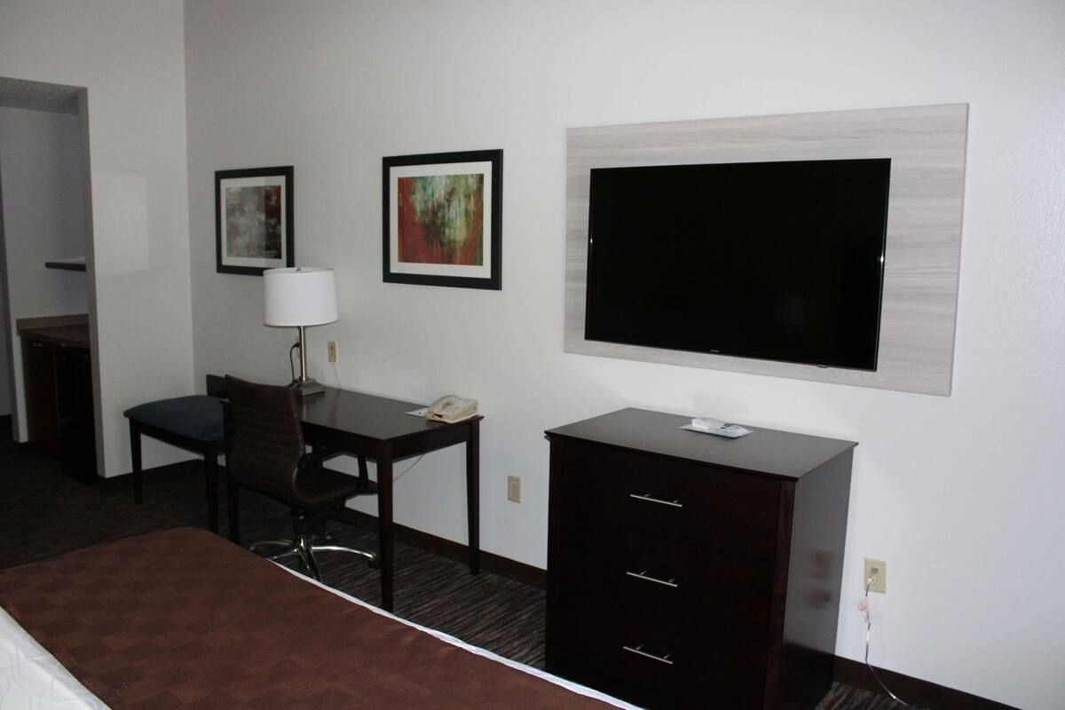 A hotel room with a bed, a desk with a lamp, a chair, a TV, and a dresser.
