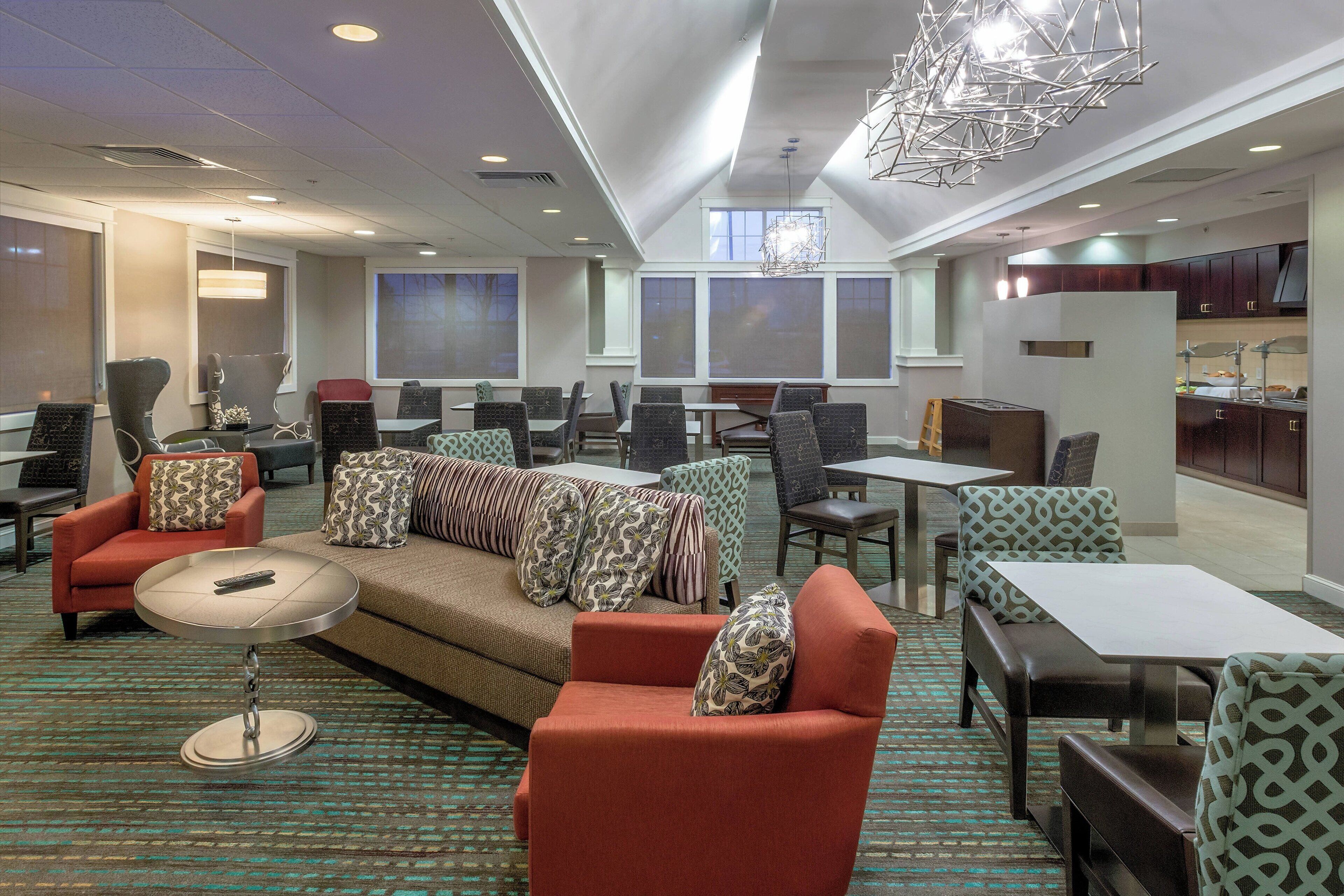Een ruime hotellobby met een hoge plafond, grote ramen en diverse zithoeken met banken, stoelen en tafels.