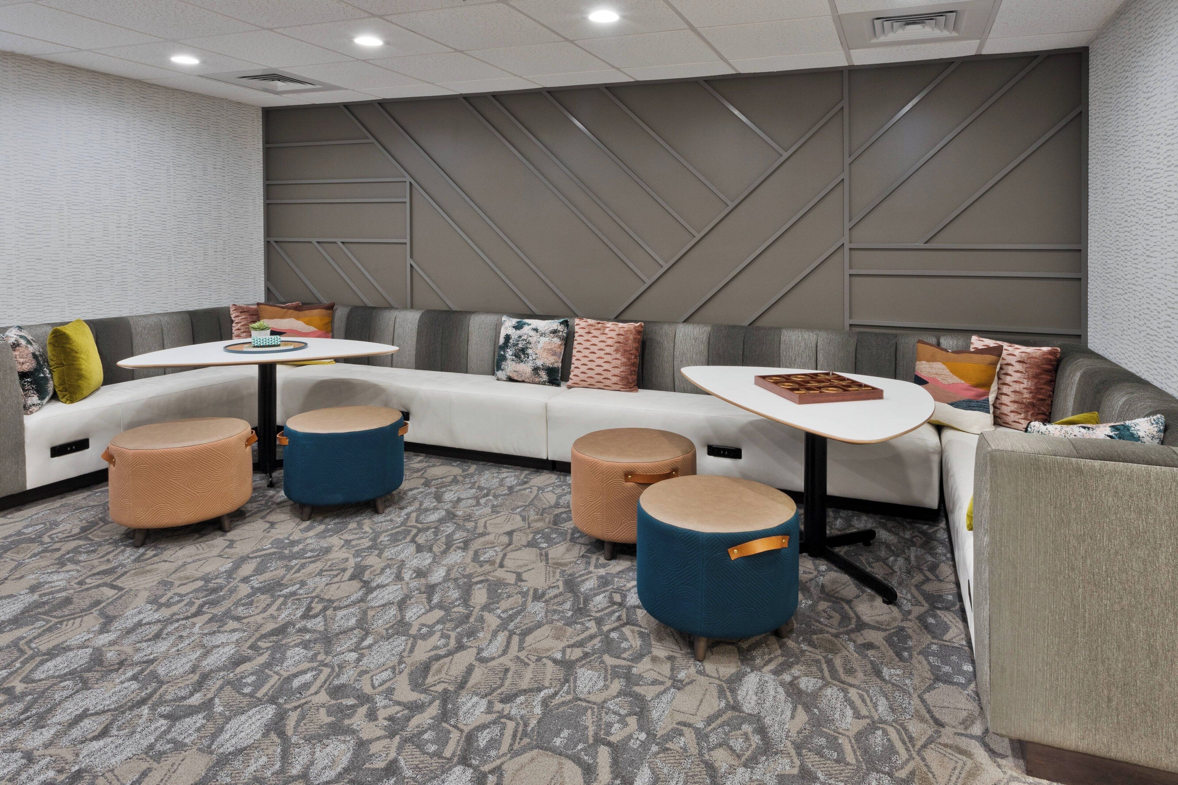 A modern lounge area with a curved white sofa, blue and beige ottomans, and a small white table.