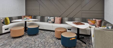 A modern lounge area with a curved white sofa, blue and beige ottomans, and a small white table.