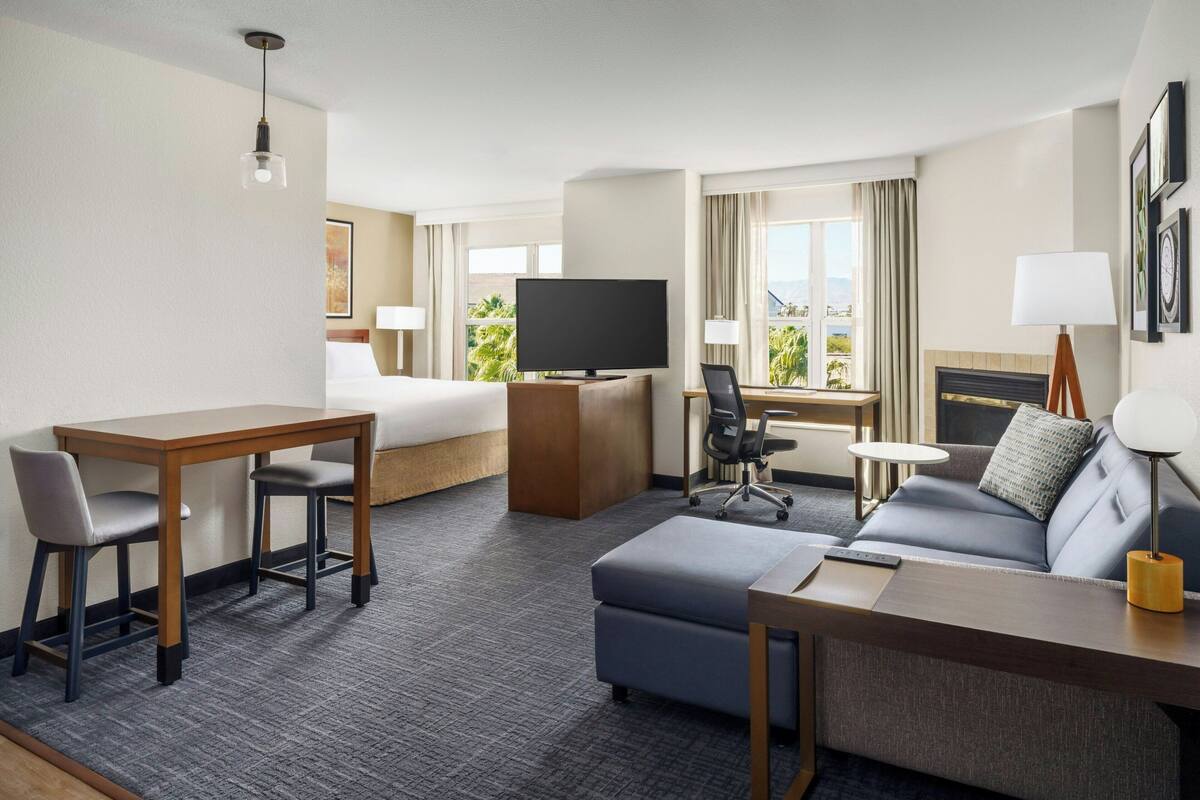 A hotel room with a bed, a desk with a computer, a sofa, and a television.