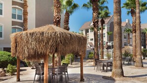 A thatched gazebo with tables and chairs, surrounded by palm trees and a building with a light-colored facade. - Residence Inn By Marriott Las Vegas Stadium Area  (Las Vegas)