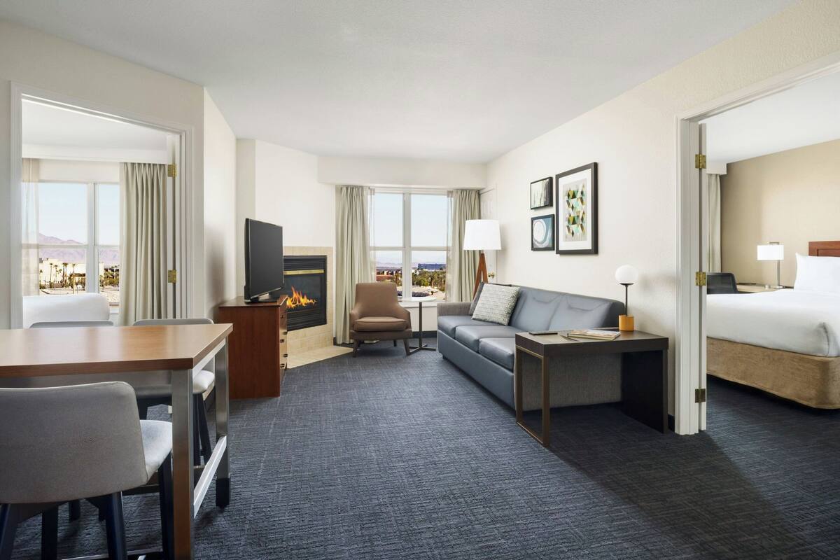 A hotel room with a bed, a sofa, a desk, a TV, and a fireplace.