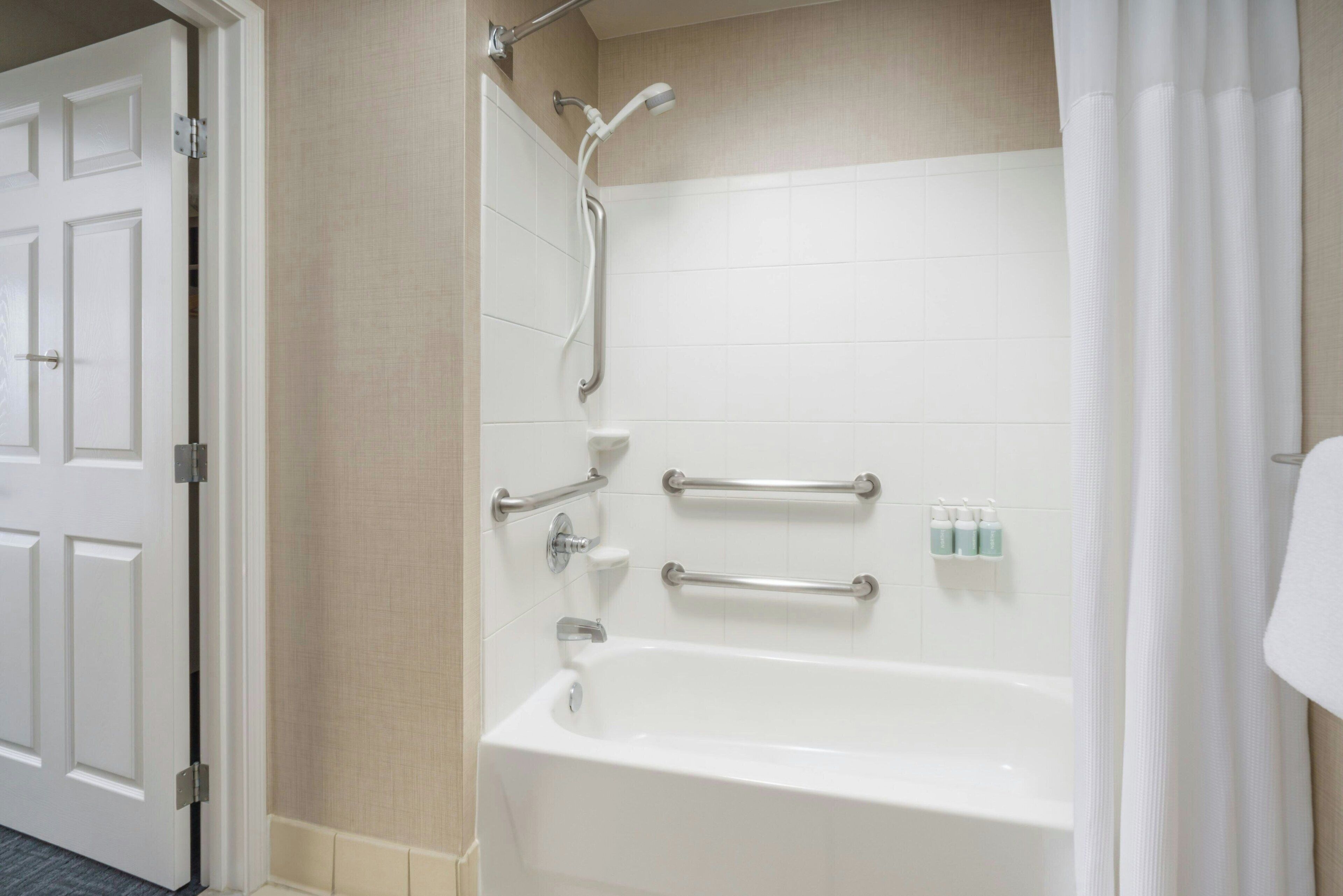 Un baño con bañera, barras de apoyo y ducha.