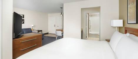 A hotel room with a large bed, a desk with a chair, a television, and a door leading to another room.
