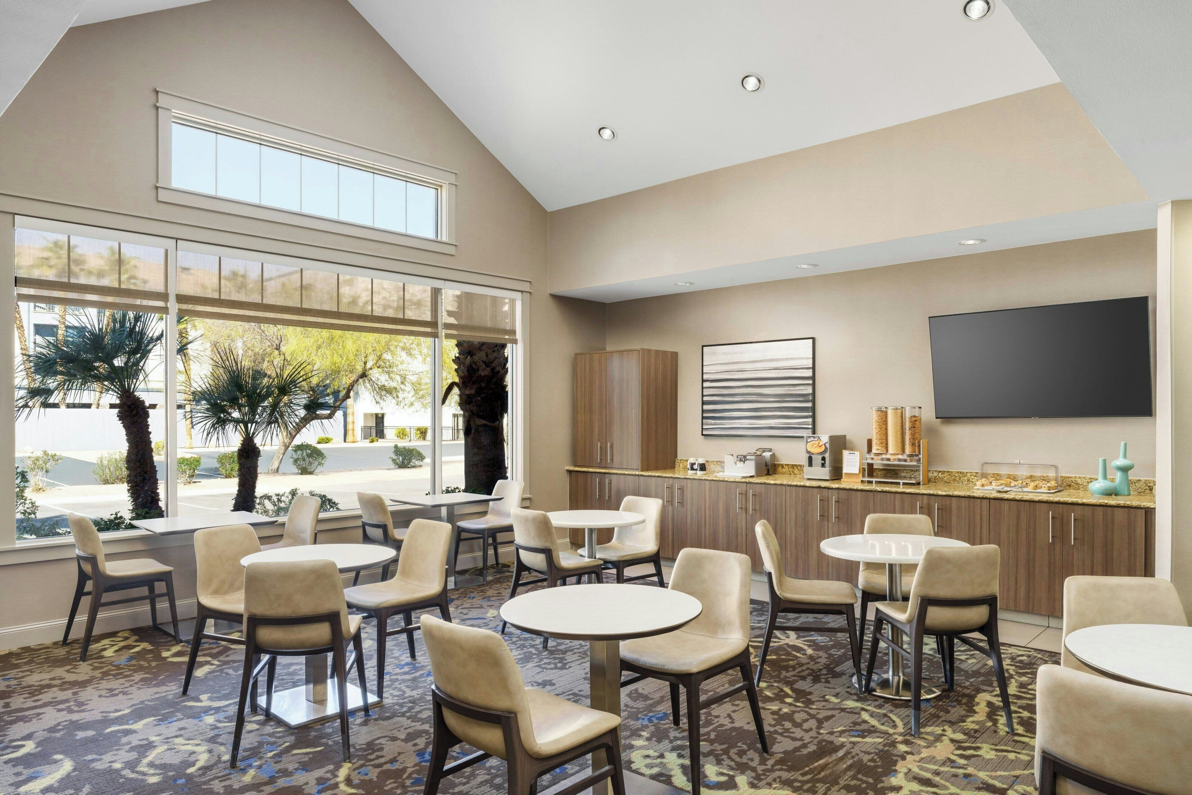 A hotel lobby with multiple seating areas, a bar, and a large TV screen.