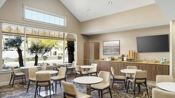 A hotel lobby with multiple seating areas, a bar, and a large TV screen.