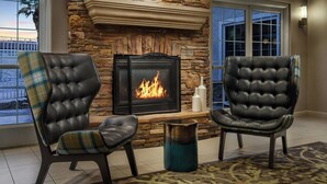 A fireplace with a stone surround, two leather armchairs with plaid upholstery, and a metal vase on a patterned rug. - Residence Inn By Marriott Las Vegas Stadium Area  (Las Vegas)
