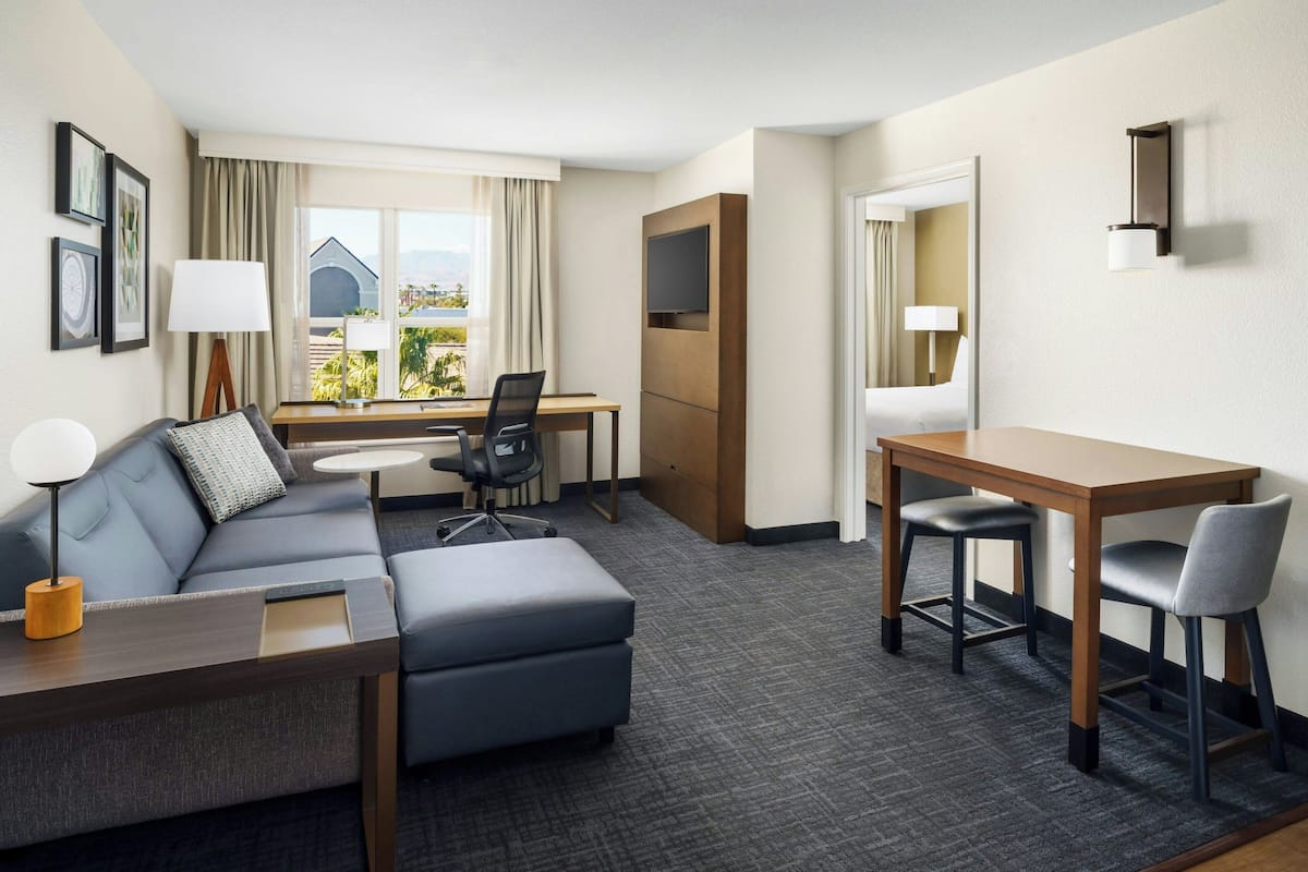 A hotel room with a sofa, a desk, a chair, a TV, and a window with curtains.