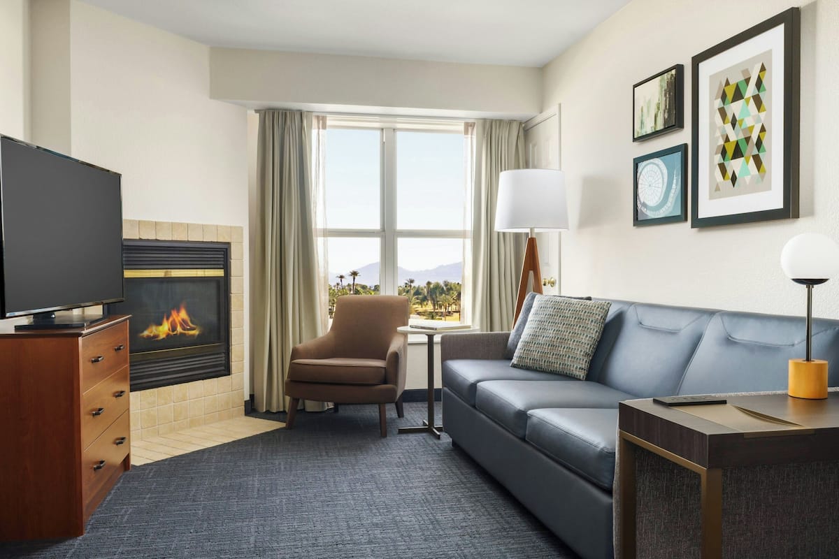 A hotel room with a fireplace, a sofa, a TV, and a desk with a lamp.