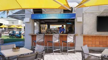 An outdoor bar area with yellow umbrellas, metal chairs, and a bartender.