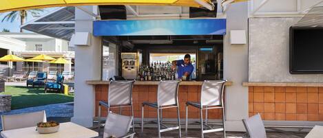 An outdoor bar area with yellow umbrellas, metal chairs, and a bartender.